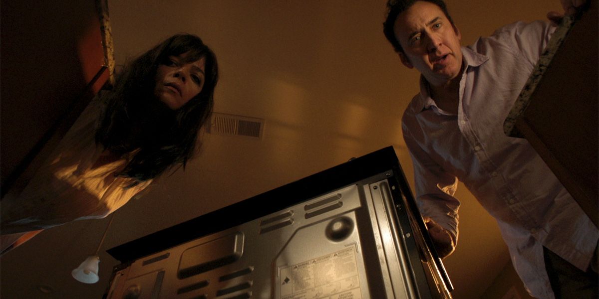 Selma Blair and Nicolas Cage looking down at something in Mom and Dad.