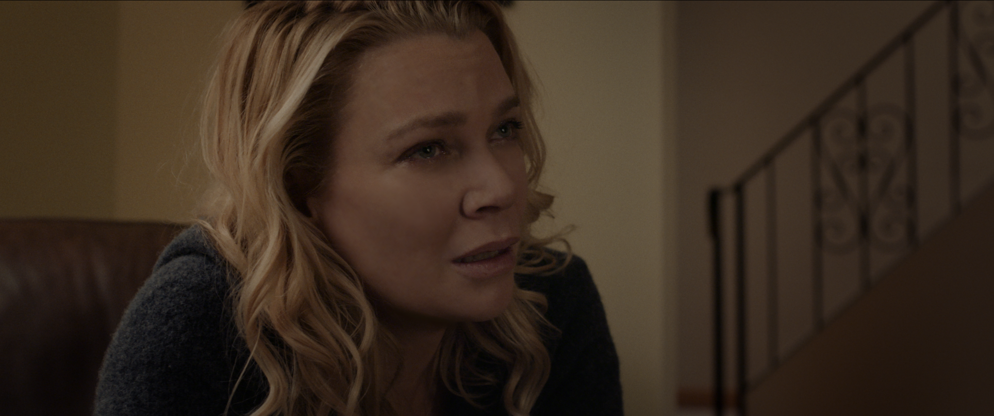 Mrs. Reyes, played by actor Laurie Holden, sits in an armchair while looking concerned in Pyewacket.