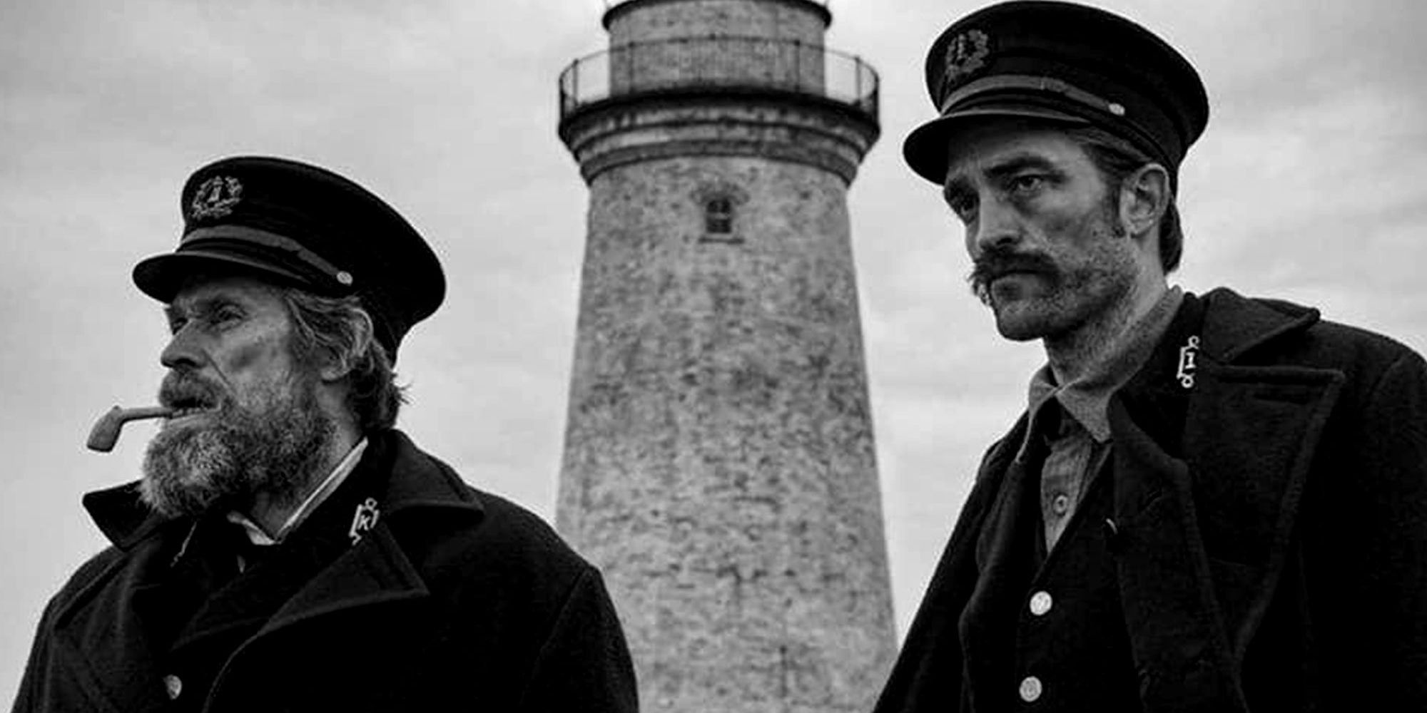 Willem Dafoe and Robert Pattinson standing in front of a lighthouse in 'The Lighthouse'