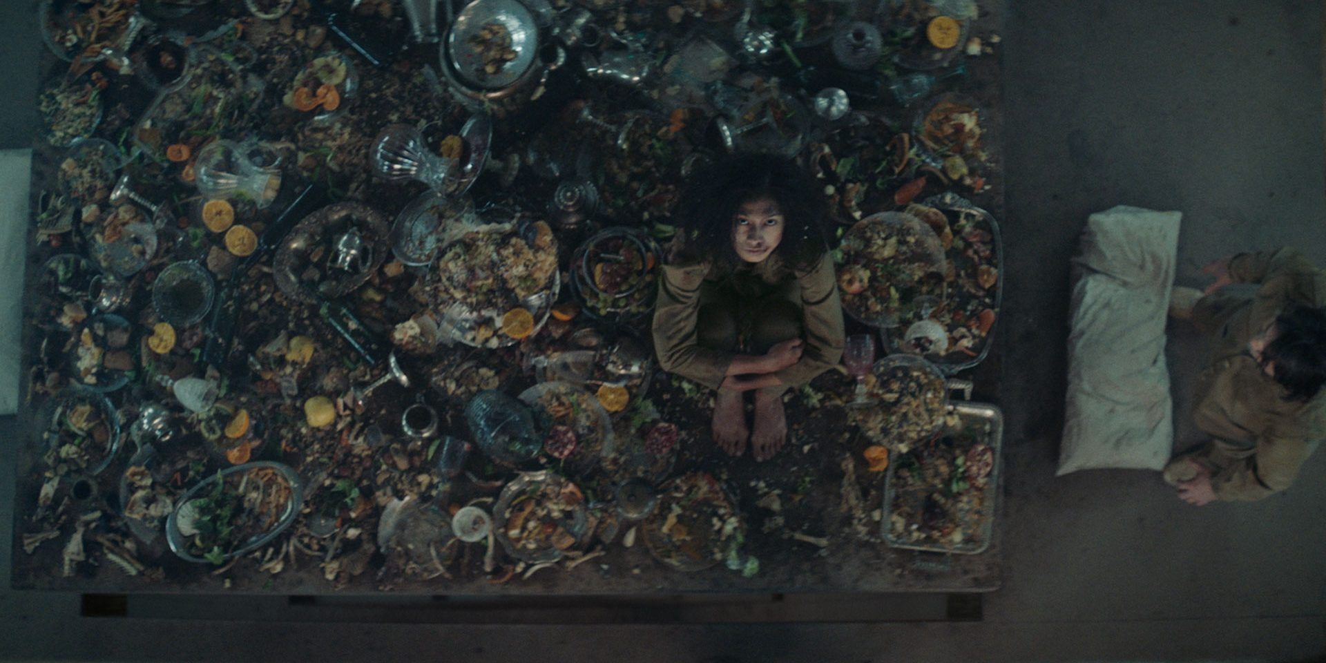 Alexandra Masangkay as Miharu sitting on a table with rotting food in The Platform (2019)