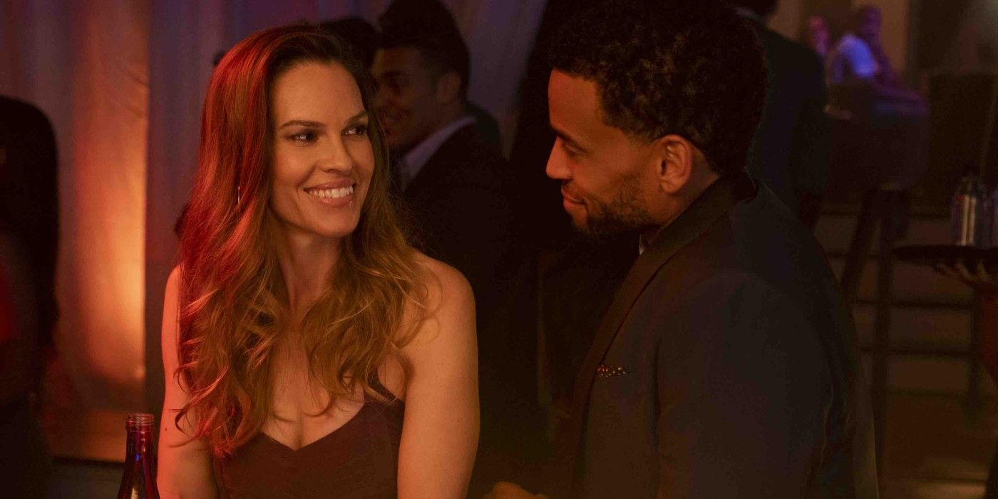 A woman in straps and a man in a jacket are looking at each other and smiling