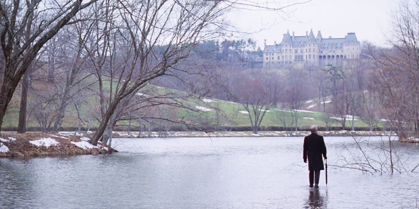 A man with an umbrella is surrounded by water and a little bit of unmelted snow on the ground in front of a mansion estate in Being There.