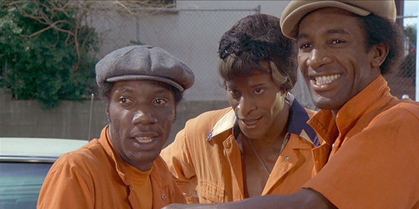 Three workers at a car wash smile as they wear orange work uniforms in Car Wash.