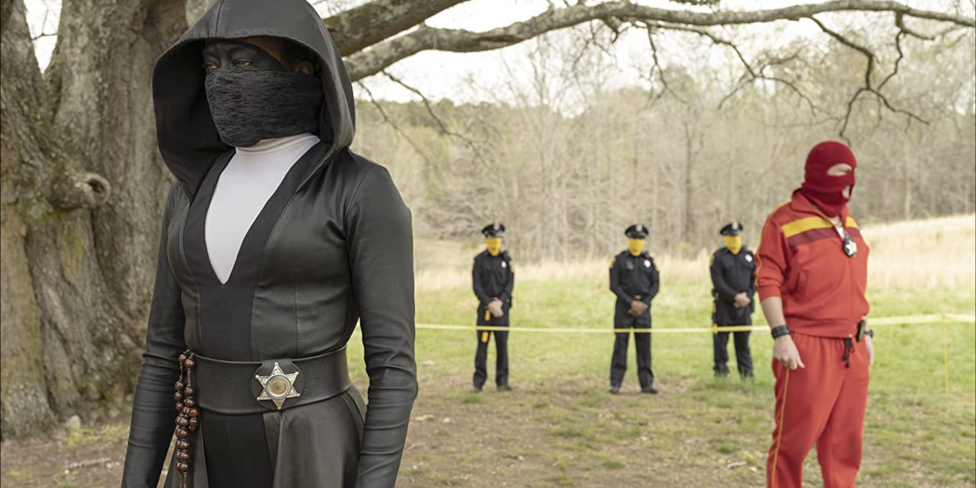 Sister Knight is standing in an open field with the cops behind her in Watchmen.