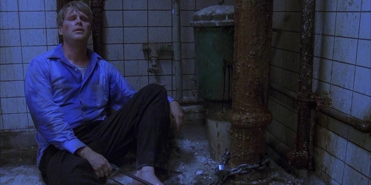 A distraught man sits on the floor in a dilapidated room in Saw