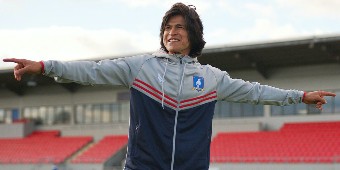 Dani with his arms outspread on the soccer field, smiling widely in a scene from Ted Lasso.