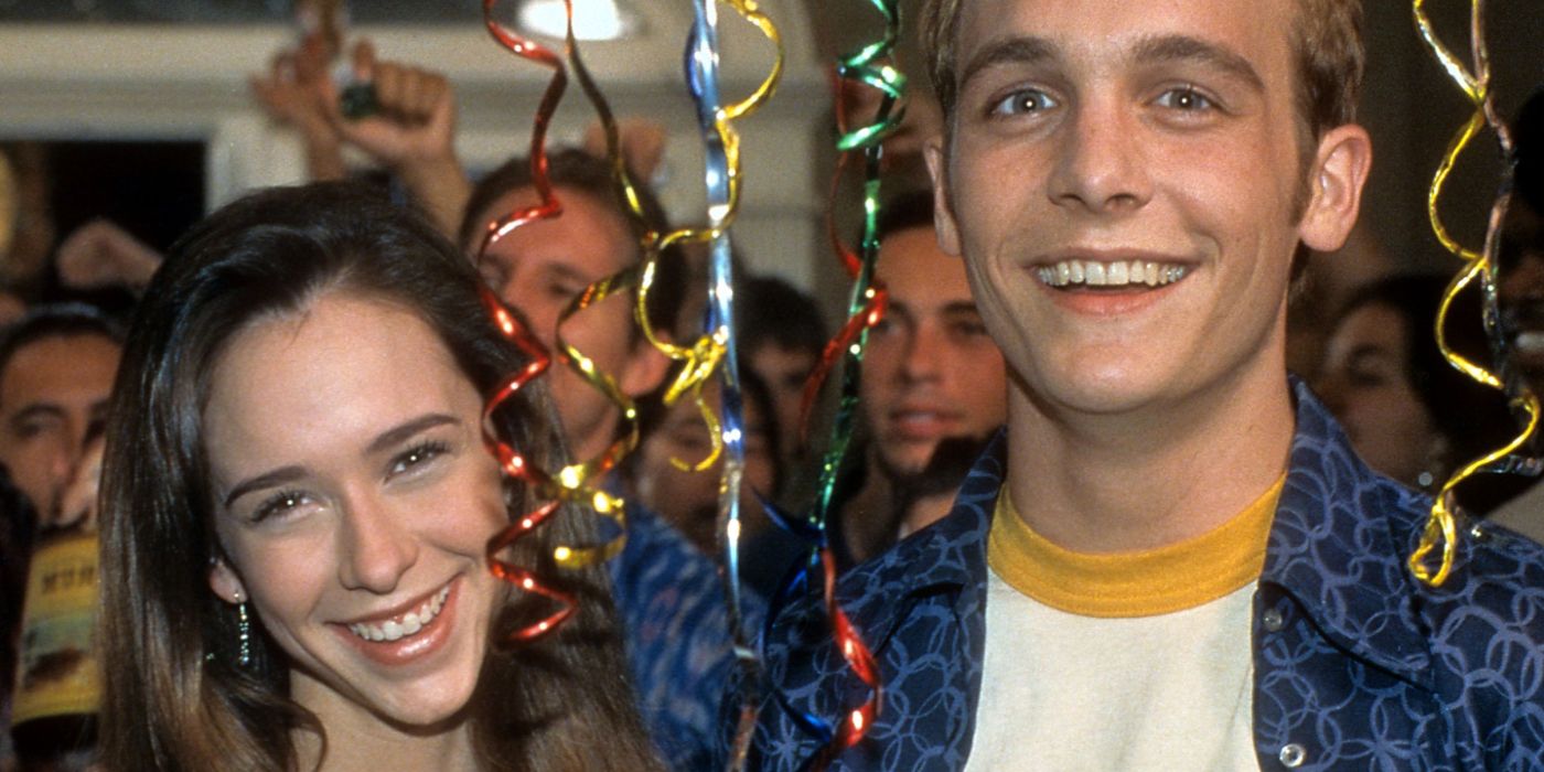 A young woman and man smiling at a party, streamers in their face in a scene from Can't Hardly Wait.