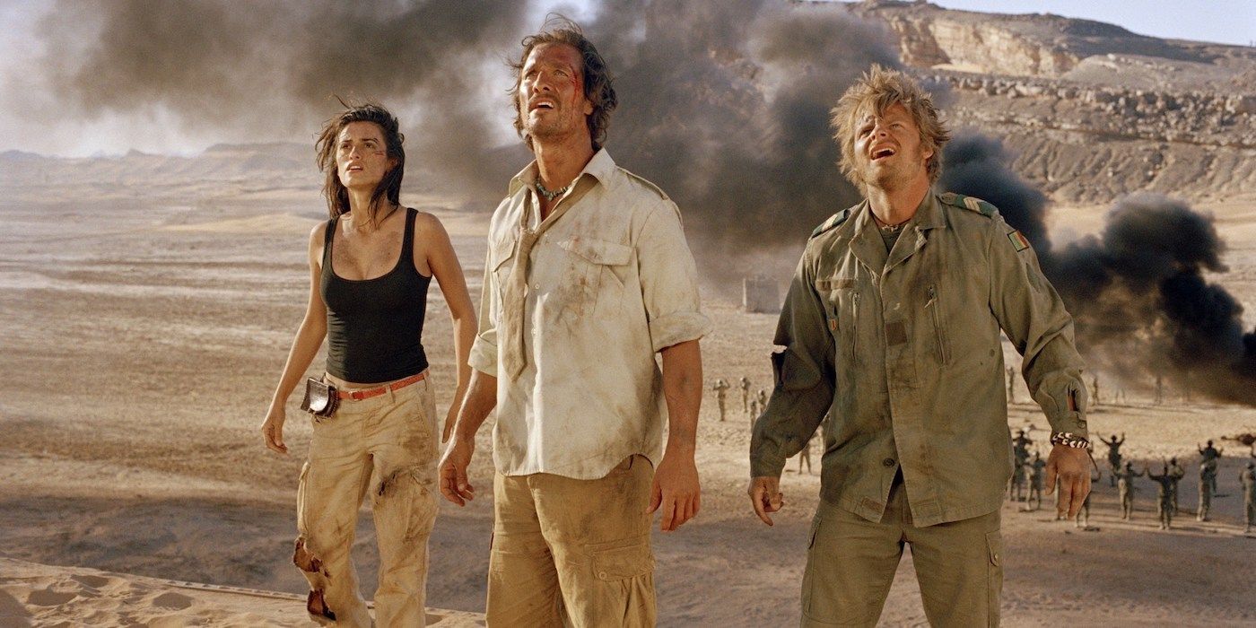 Three bloodied explorers stand in the desert with smoke wafting behind them.