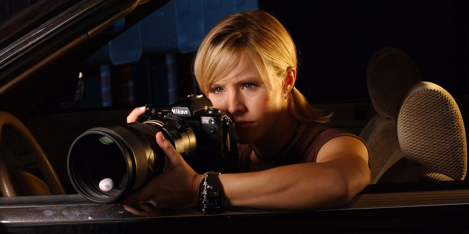 Veronica Mars sitting in a car holding a DSLR with a long lens