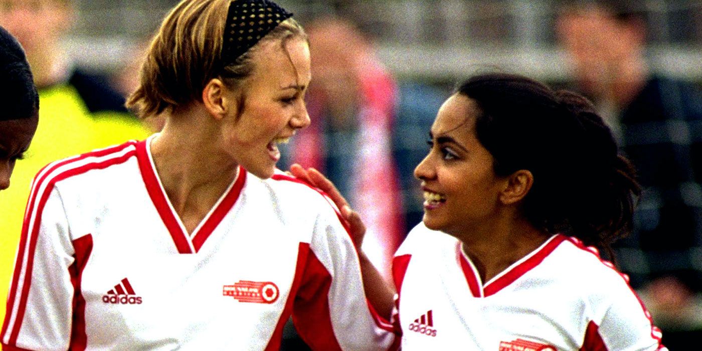 Jess and Juliette smiling at each other while on the football field in Bend It Like Beckham