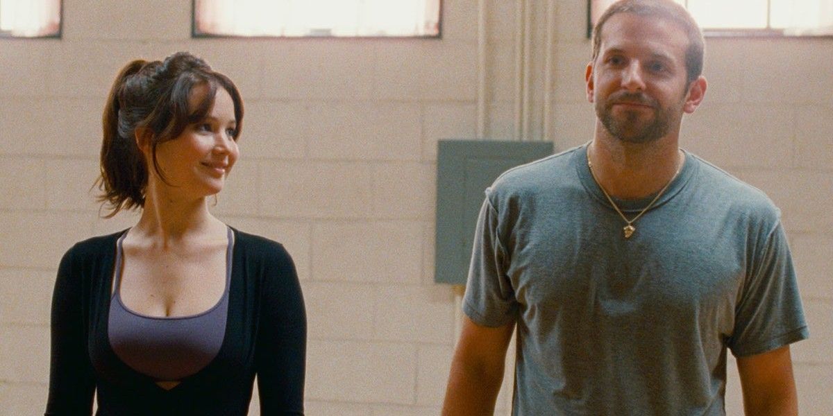 Jennifer Lawrence and Bradley Cooper as Tiffany and Pat standing side by side and smiling in Silver Linings Playbook.