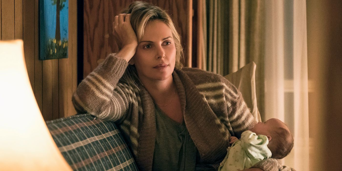 Charlize Theron as Marlo sitting on a couch holding a baby in Tully