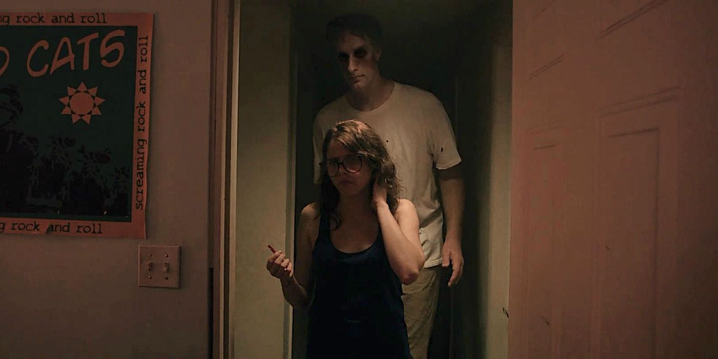 A tall, ghostly man standing behind a teenager in It Follows
