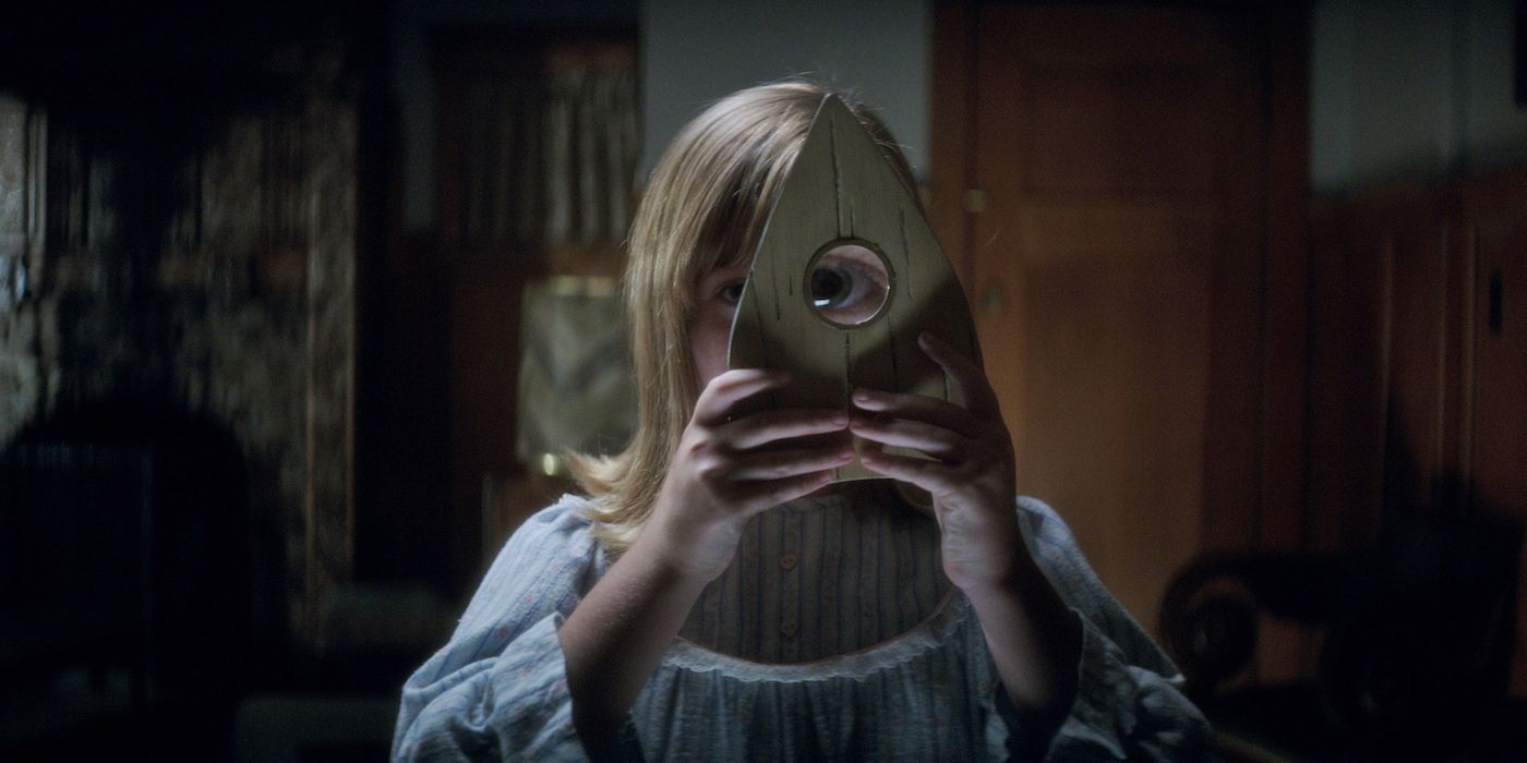 Lulu Wilson holding a Ouija planchette over her eye in Ouija: Origin of Evil