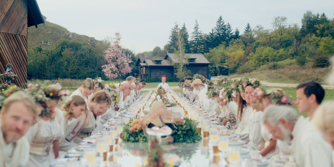 Several cast members in white sitting in a long table to eat a feast in 'Midsommar'.