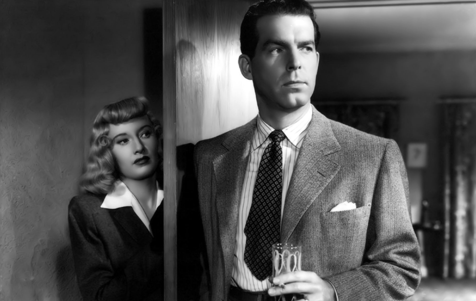 Fred MacMurray standing in a door way and Barbara Stanwyck is hiding behind the door in Double Indemnity