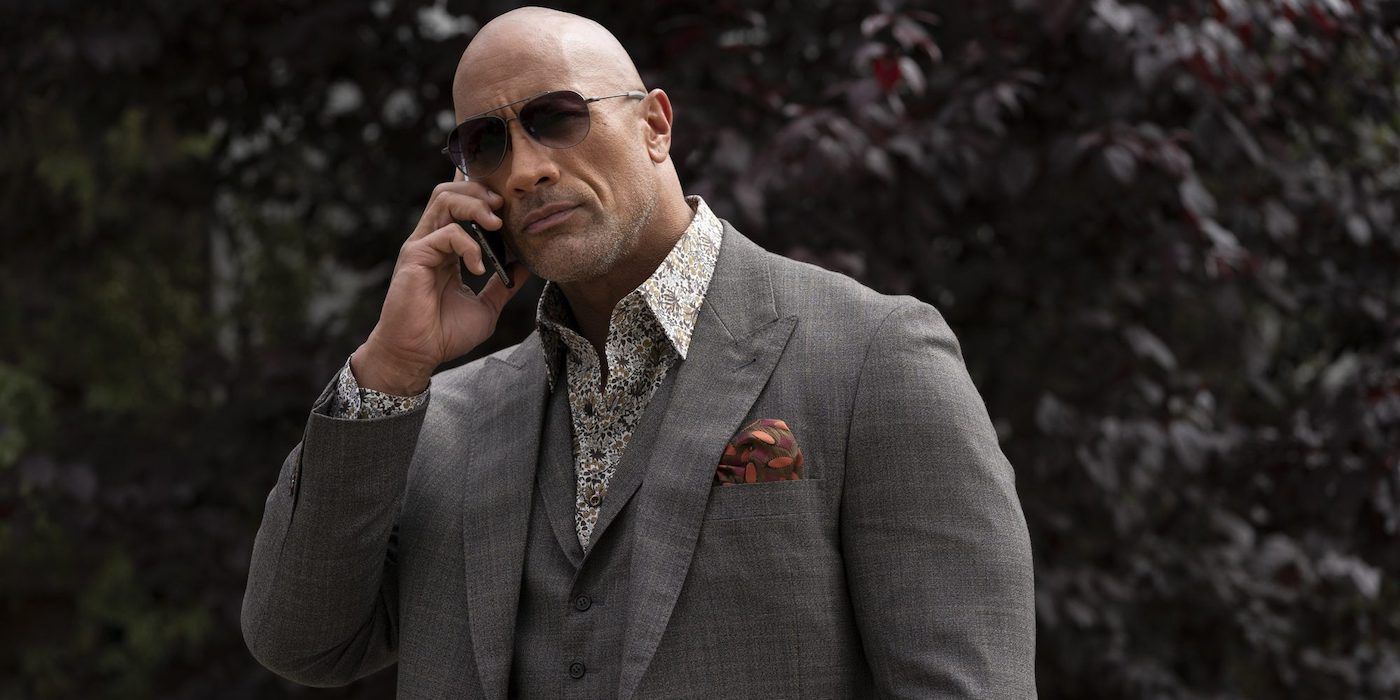 Dwayne Johnson in a suit and sunglasses talks on the phone in Ballers.