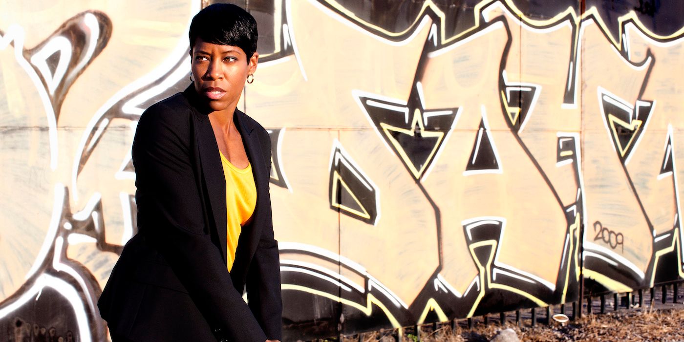 Regina King brandishes her service weapon as she stands in front of graffiti-covered wall in the series Southland
