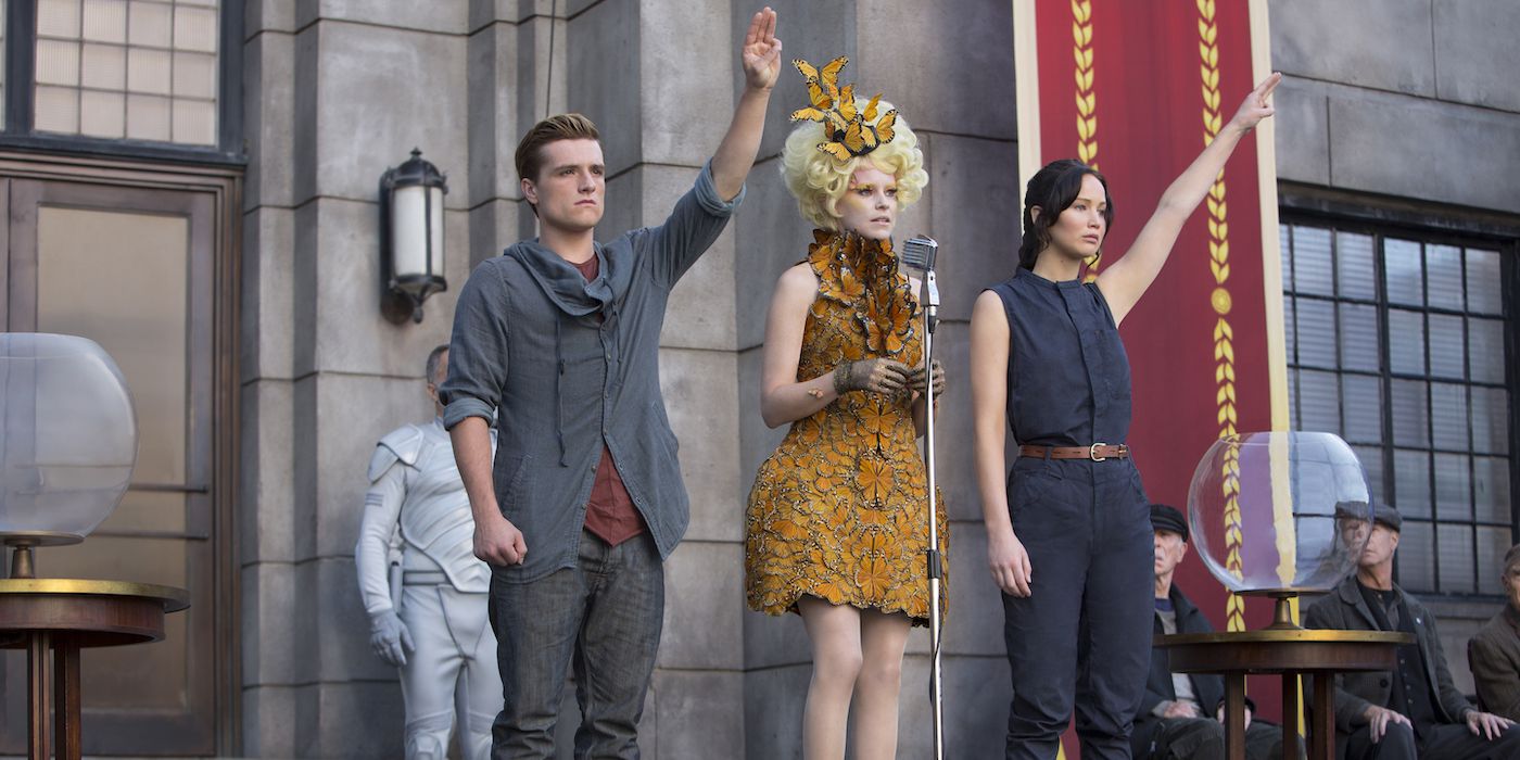 Peeta and Katniss doing the Mockingjay symbol while Effie stands between them in The Hunger Games: Catching Fire