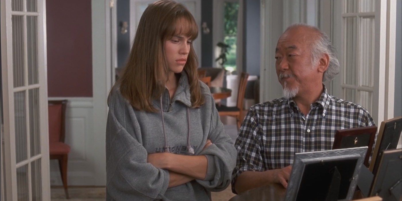 Hilary Swank as Julie Pierce standing with her arms crossed as Pat Morita as Mr. Miyagi shows her pictures in The Next Karate Kid