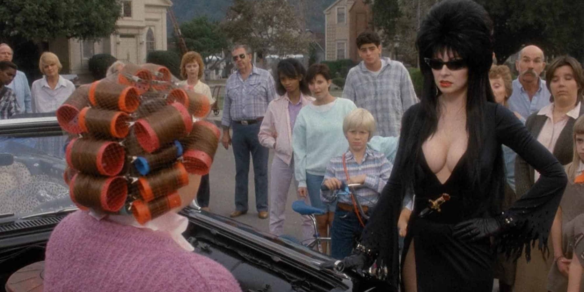 A woman with curlers in her hair in a car looking at Elvira wearing sunglasses in Elvira, Mistress of the Dark
