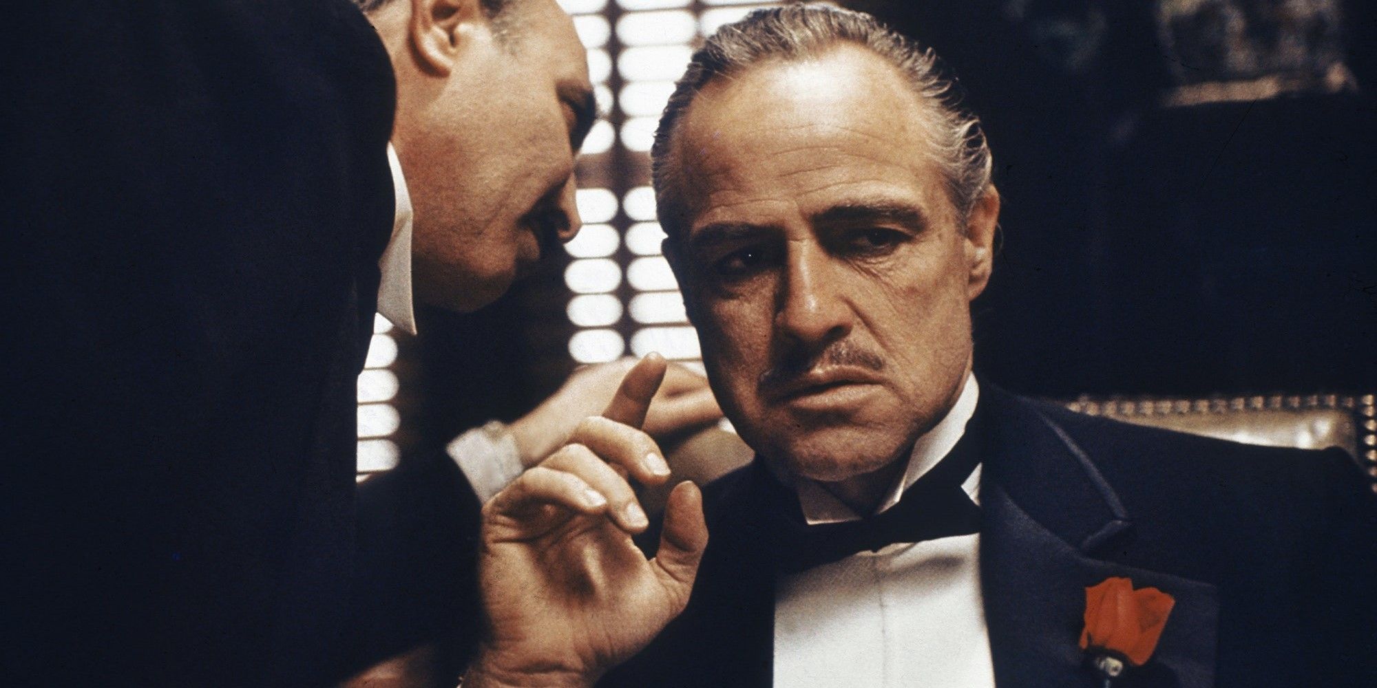 Un homme qui chuchote à l'oreille de Don Vito Corleone dans Le Parrain.