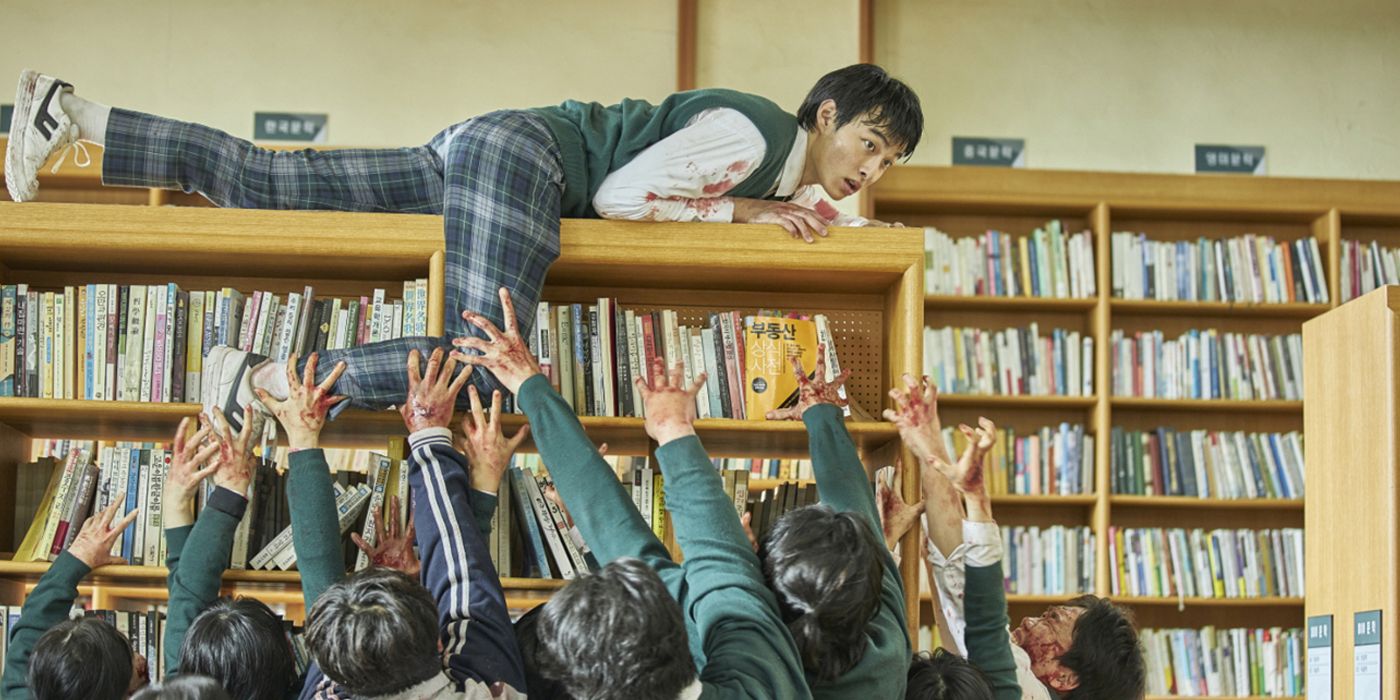 Cheong-san crawls atop a library bookcase while zombies below reach for him