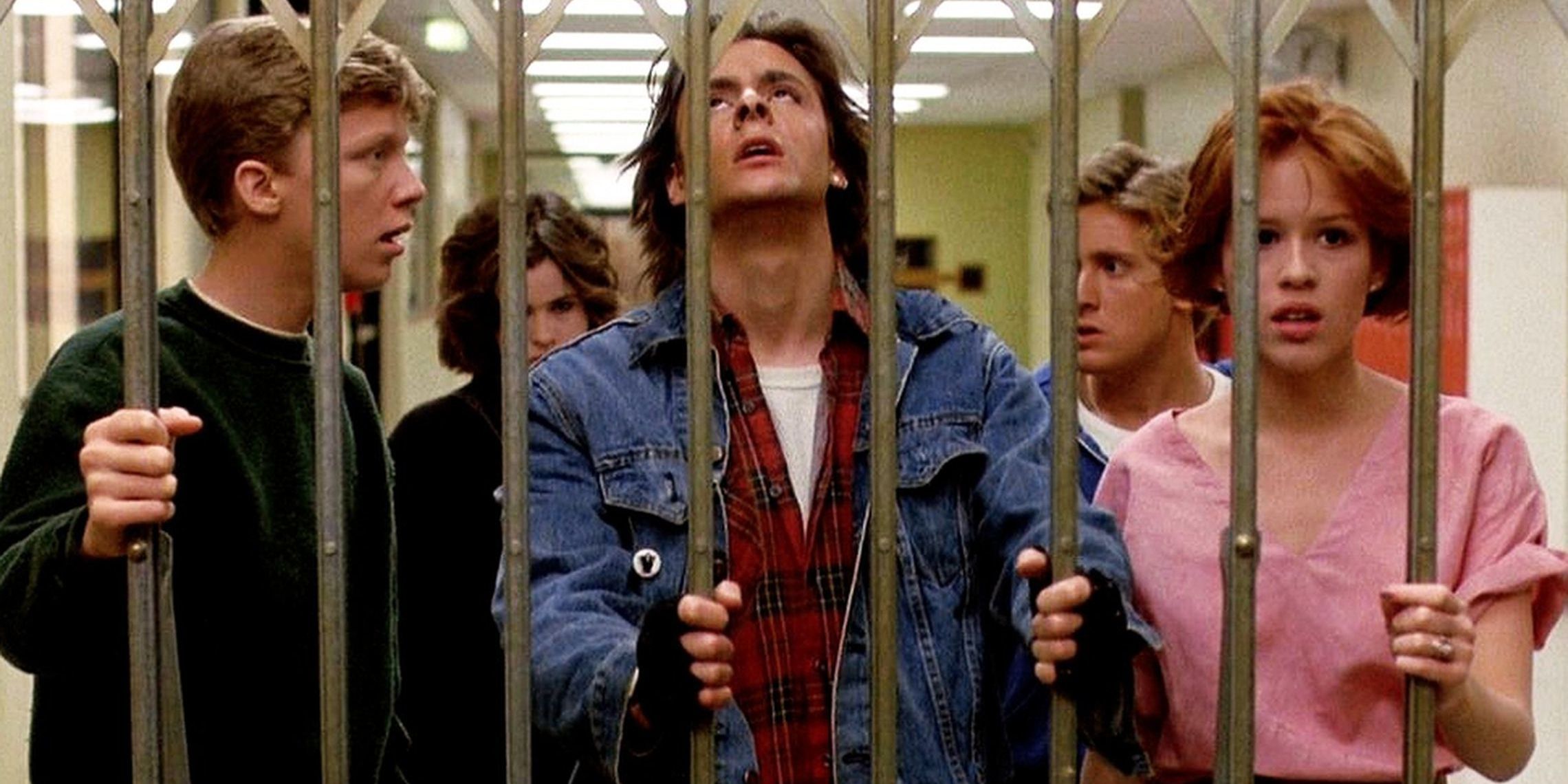 The group of teens in The Breakfast Club stand behind bars looking distraught.