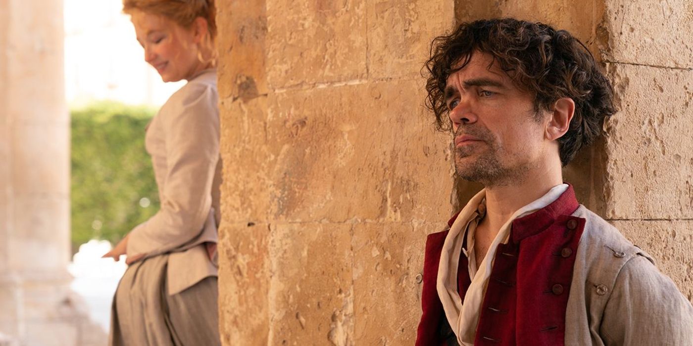 Peter Dinklage standing against a brick wall in Cyrano