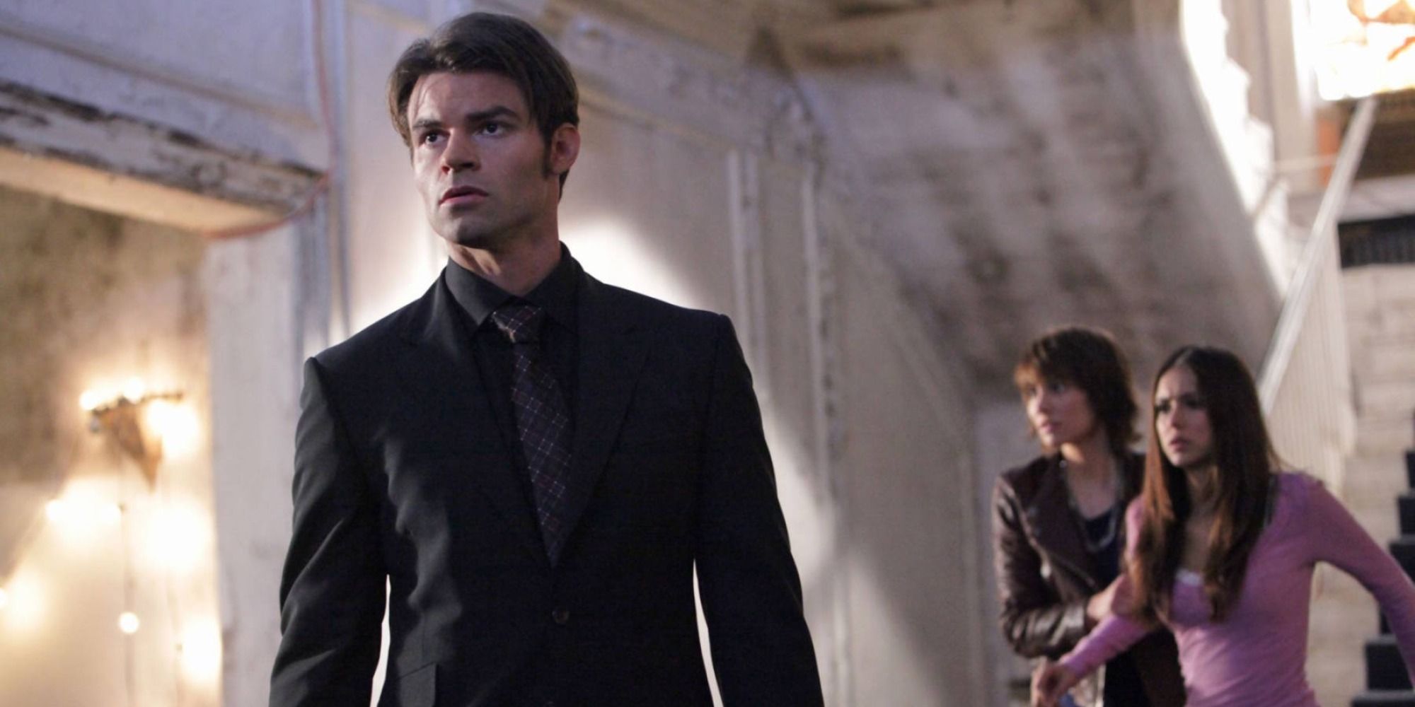 Elijah stands in the foreground while Rose holds Elena captive in the background of an episode of The Vampire Diaries