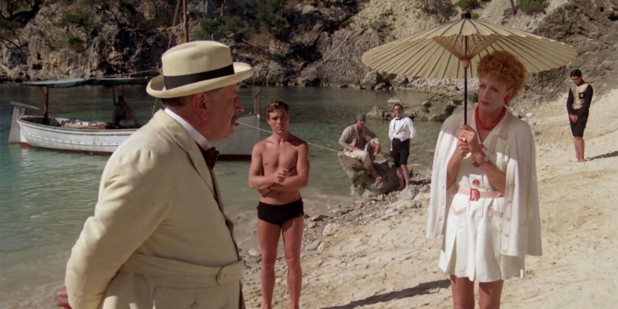 A man in a suit talks to a woman on a beach holding and umbrella