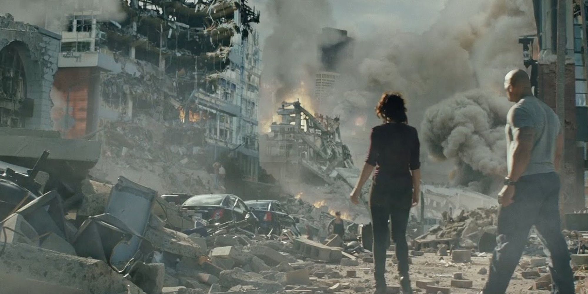 A man and woman look at a crumbled city in the aftermath of an earthquake