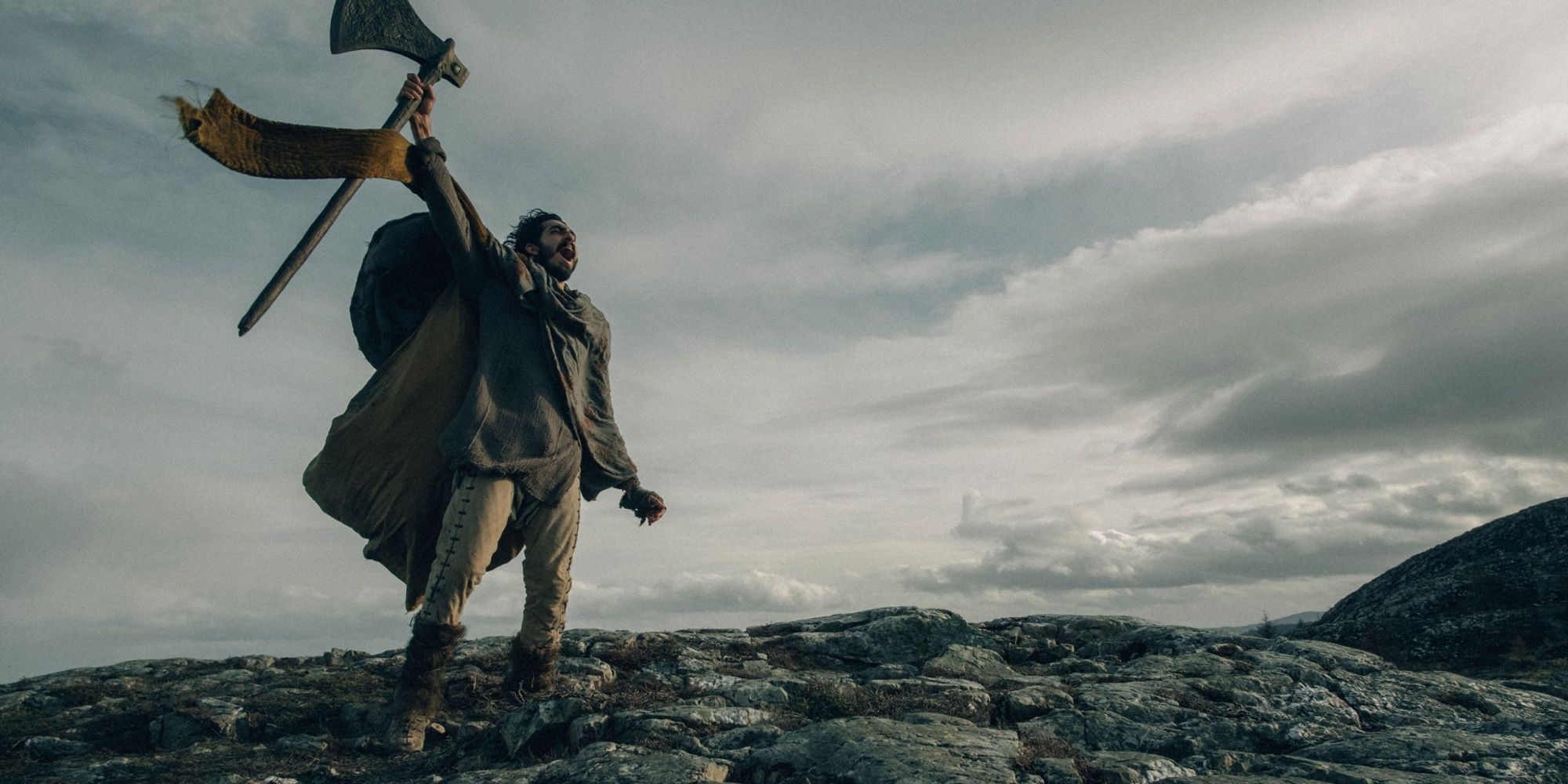 Dev Patel as Sir Gawain in 'The Green Knight' holding a big axe.