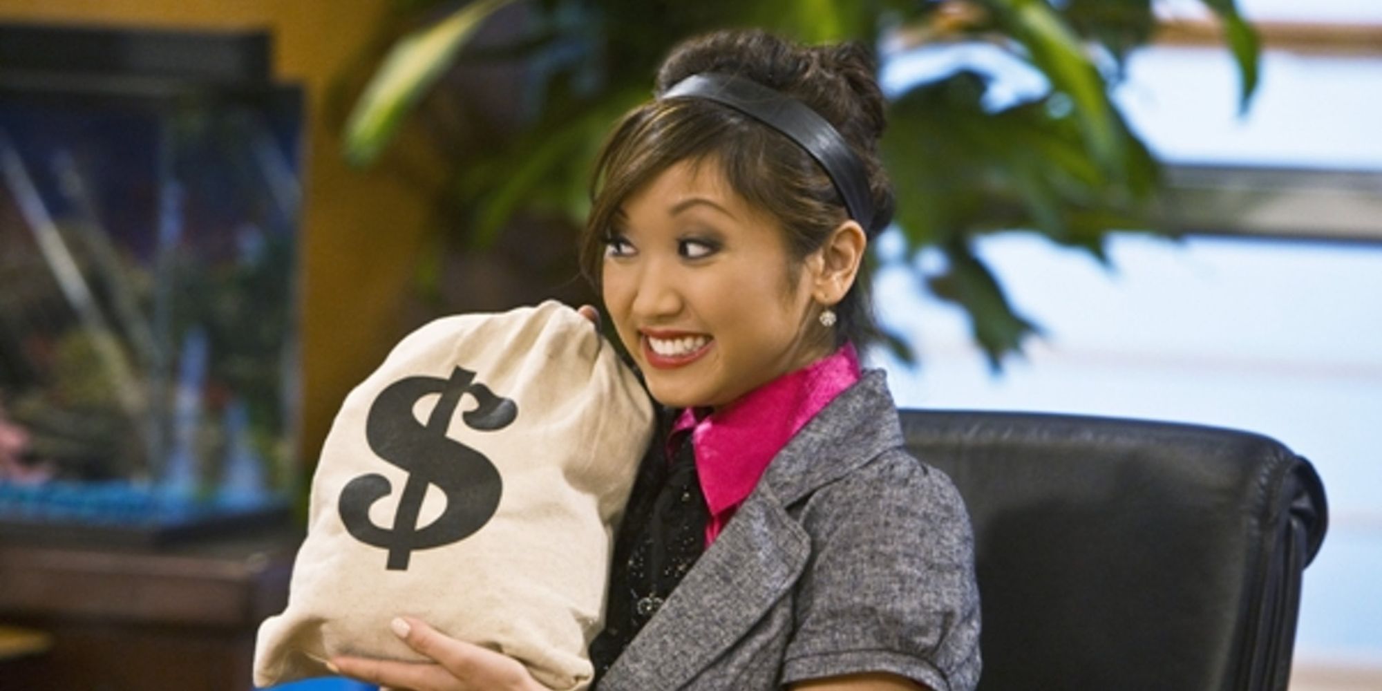Brenda Song as London Tipton holds a bag with a dollar sign on it and smiles in The Suite Life of Zack and Cody.