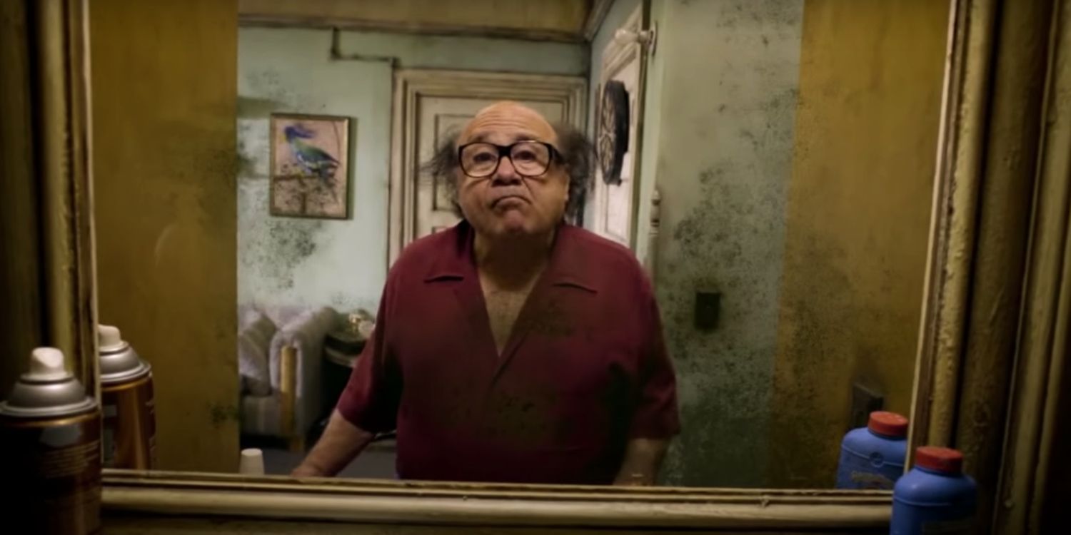 Danny DeVito looks in the mirror with a burgundy shirt & black glasses in It's Always Sunny in Philadelphia. 