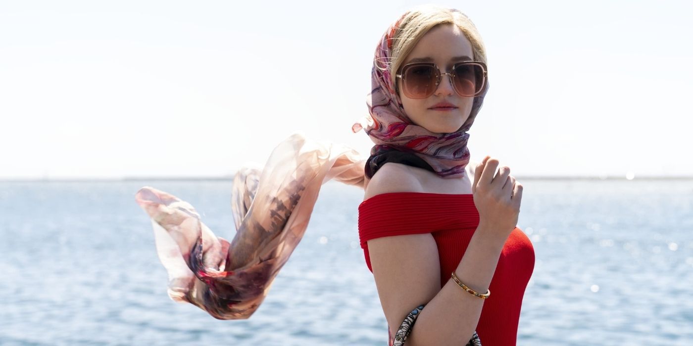 Julia Garner as Anna Delvey standing in front of the ocean wearing a red dress and colorful head scarf in 'Inventing Anna'