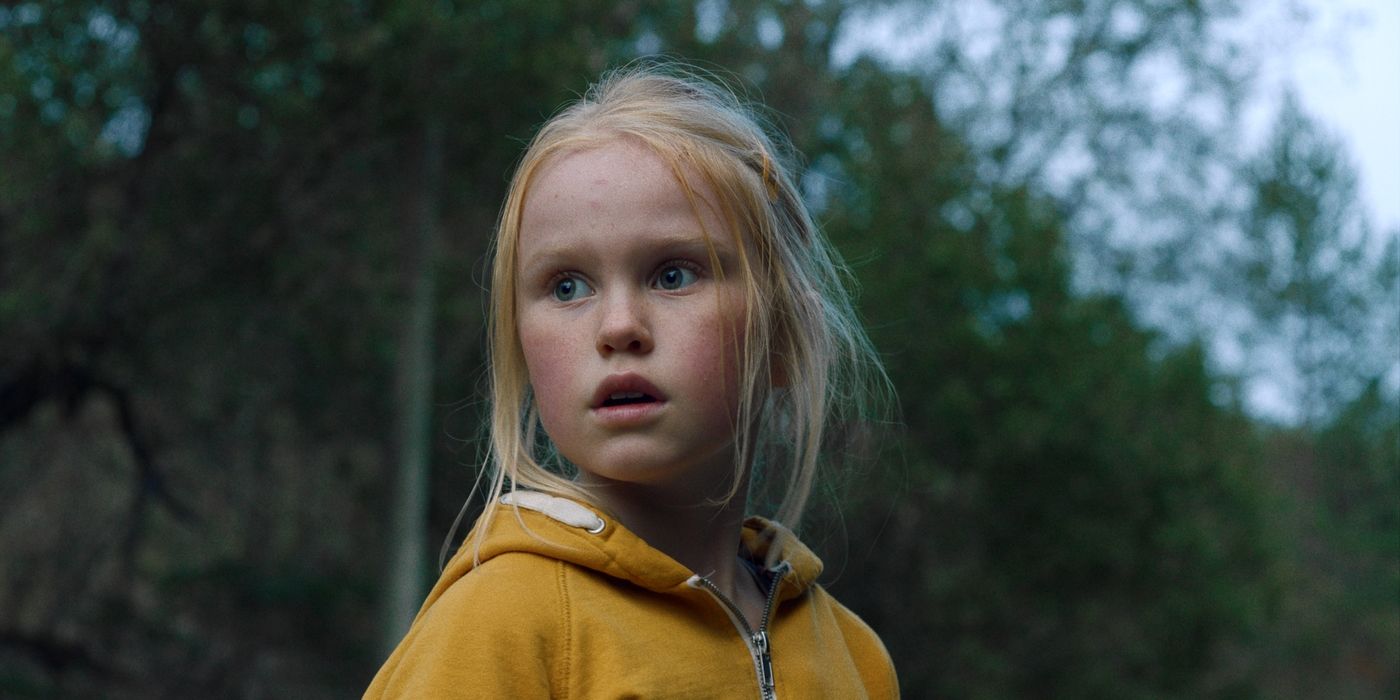 A young blonde girl in a yellow jacket looking at something, worried