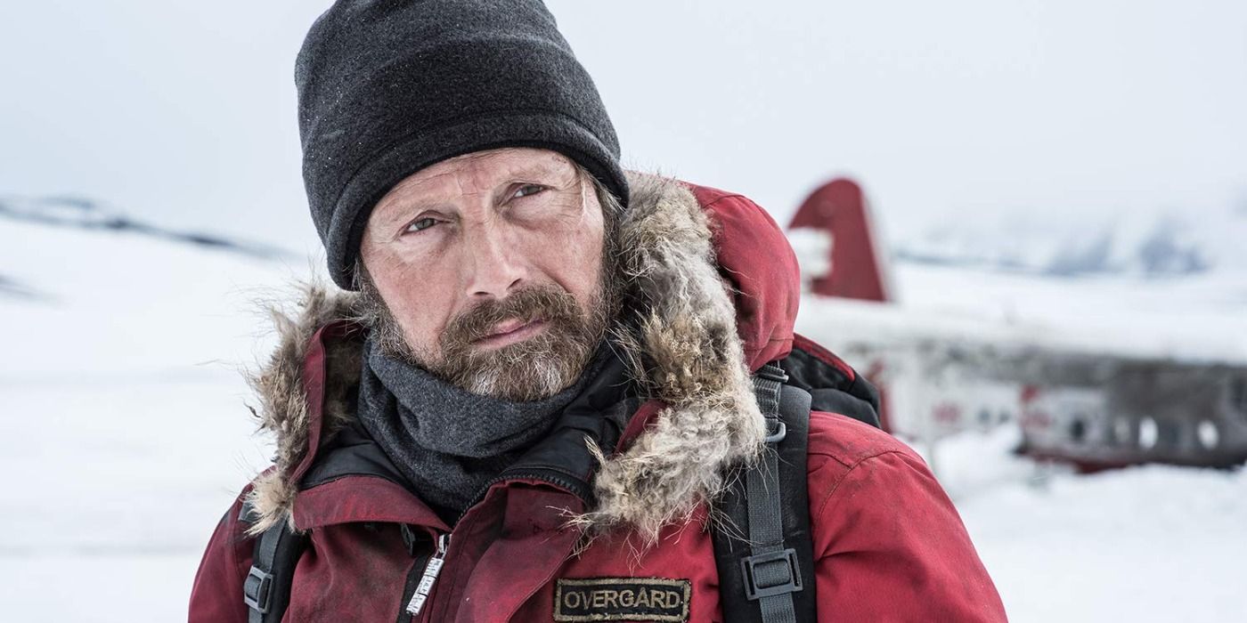 Mads Mikkelsen portant une veste d'hiver rouge et un bonnet noir dans Arctic.