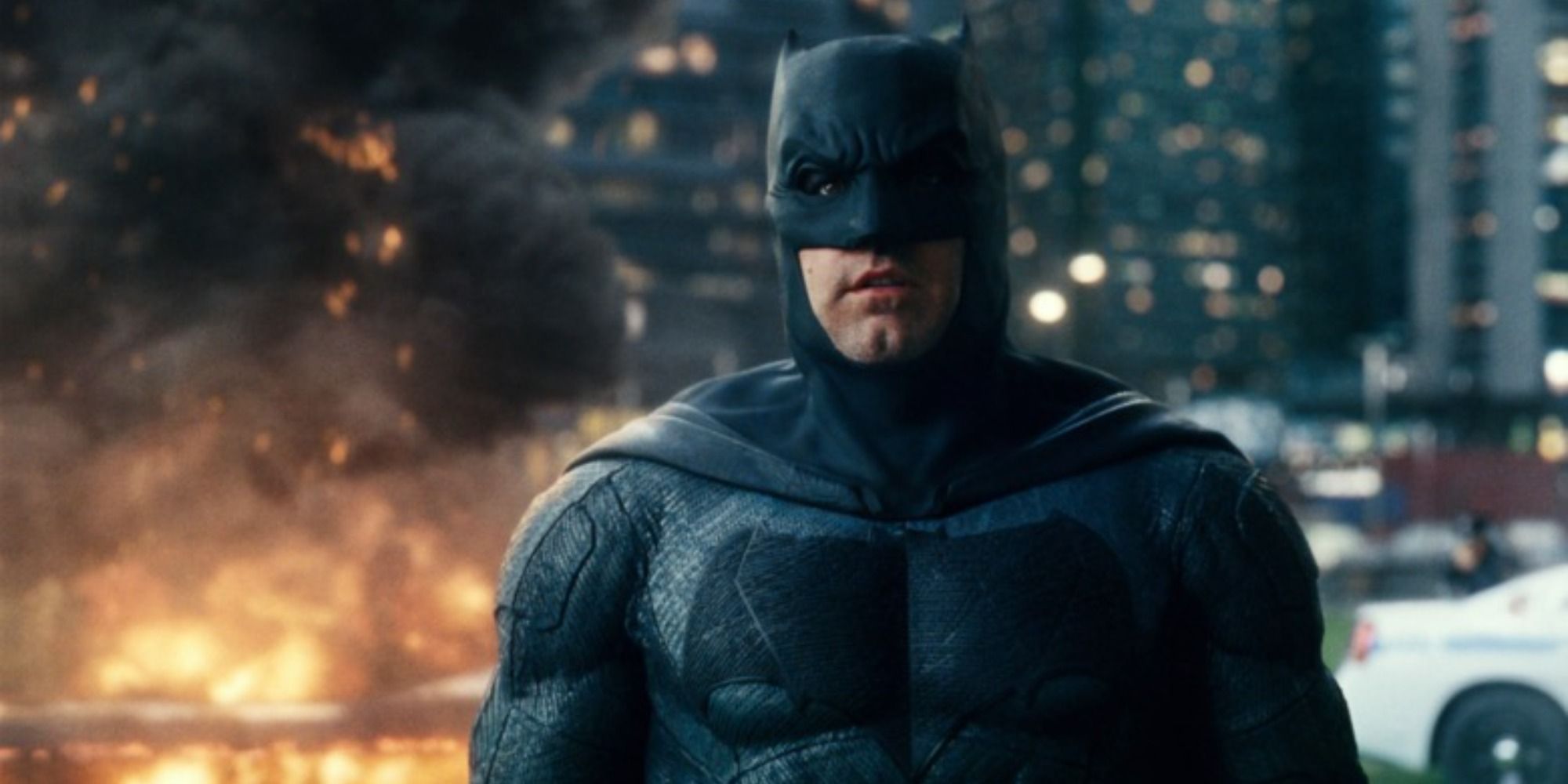 Batman looking ahead while an explosion rages behind him in Justice League