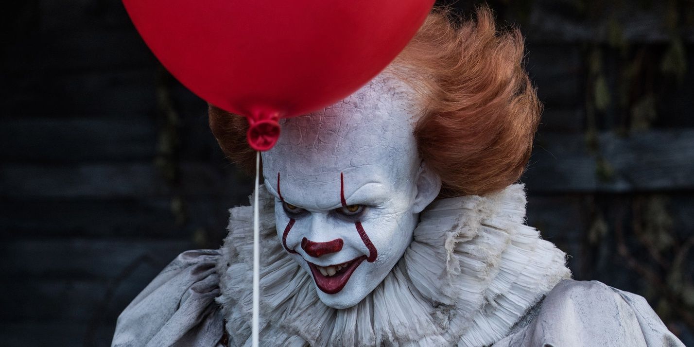 It: Bill Skarsgård as Pennywise who is holding a red balloon.