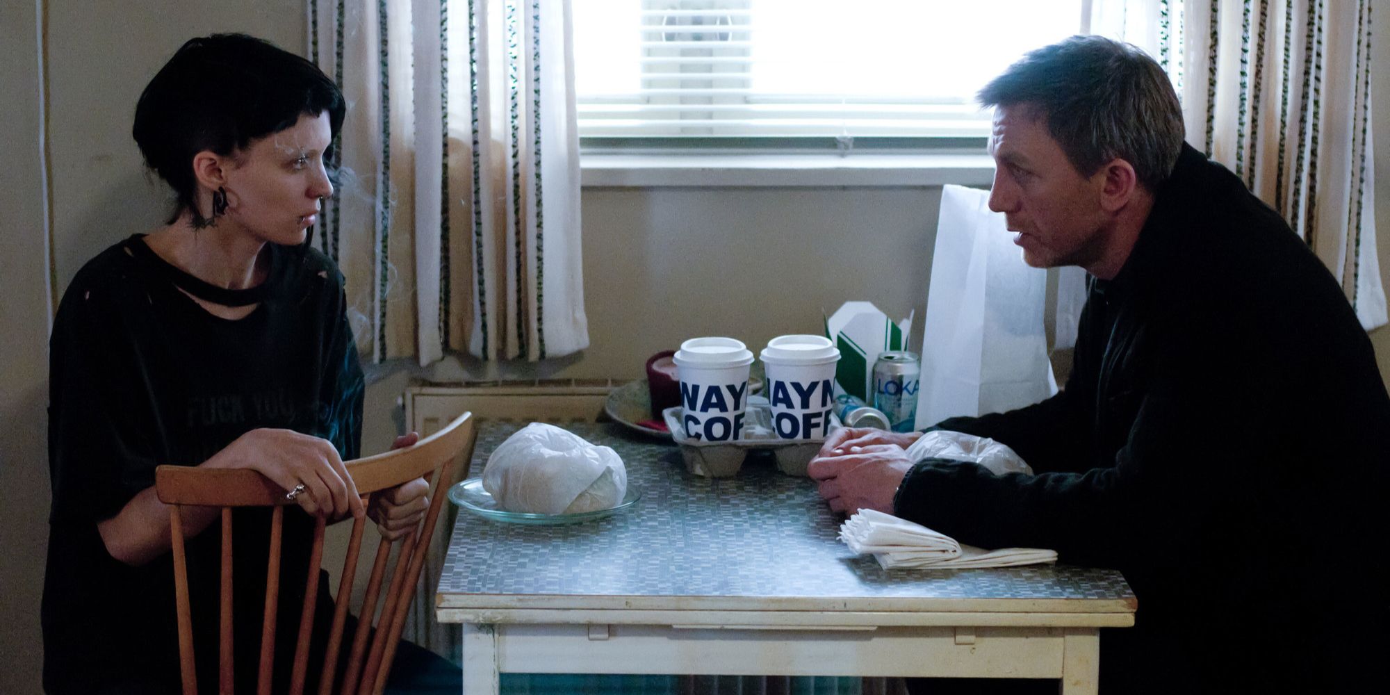 Rooney Mara and Daniel Craig sit at a table with coffee in The Girl With the Dragon Tattoo