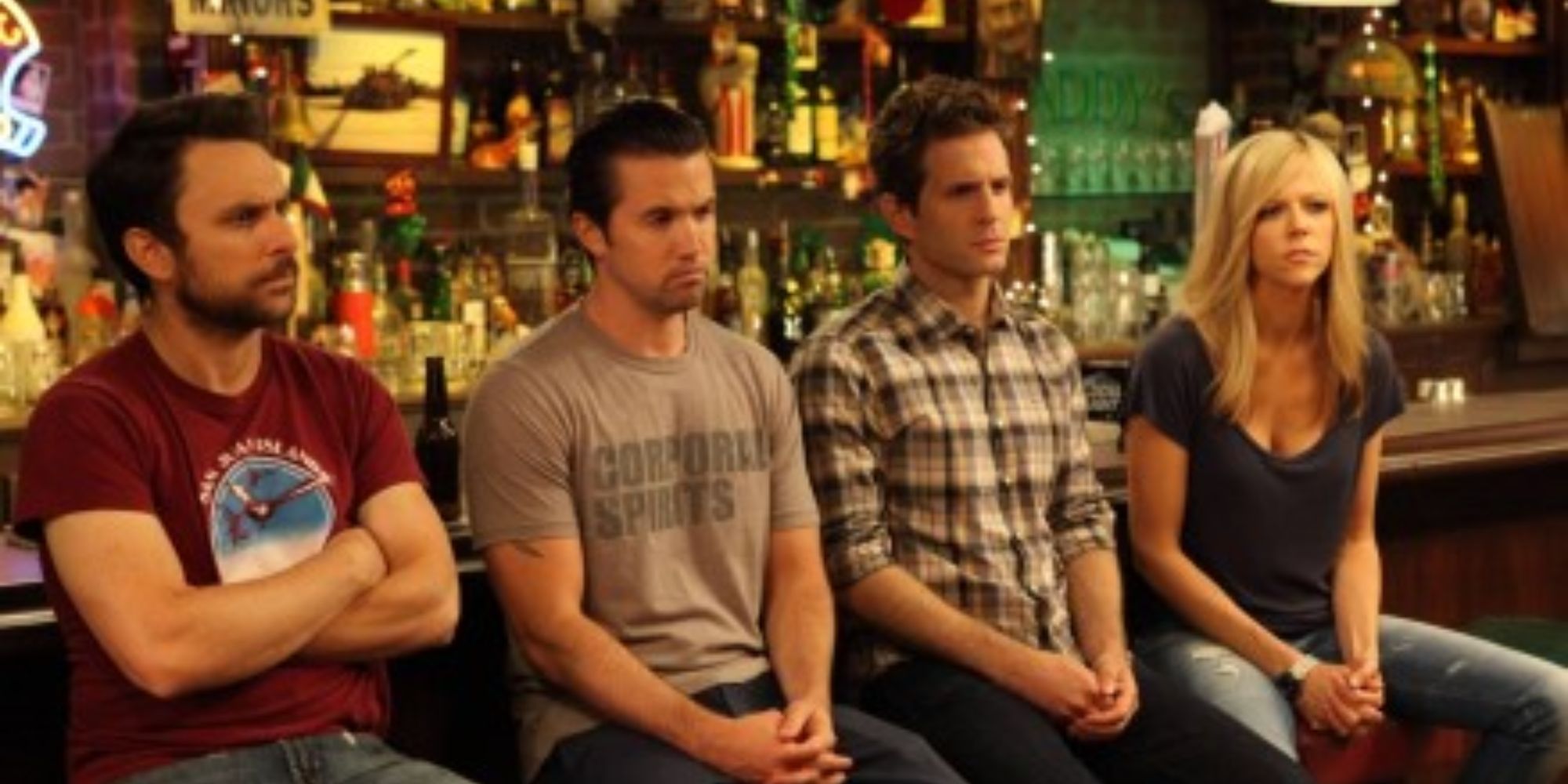 Four friends from It's Always Sunny in Philadelphia sitting on barstools in the bar, looking despondent.