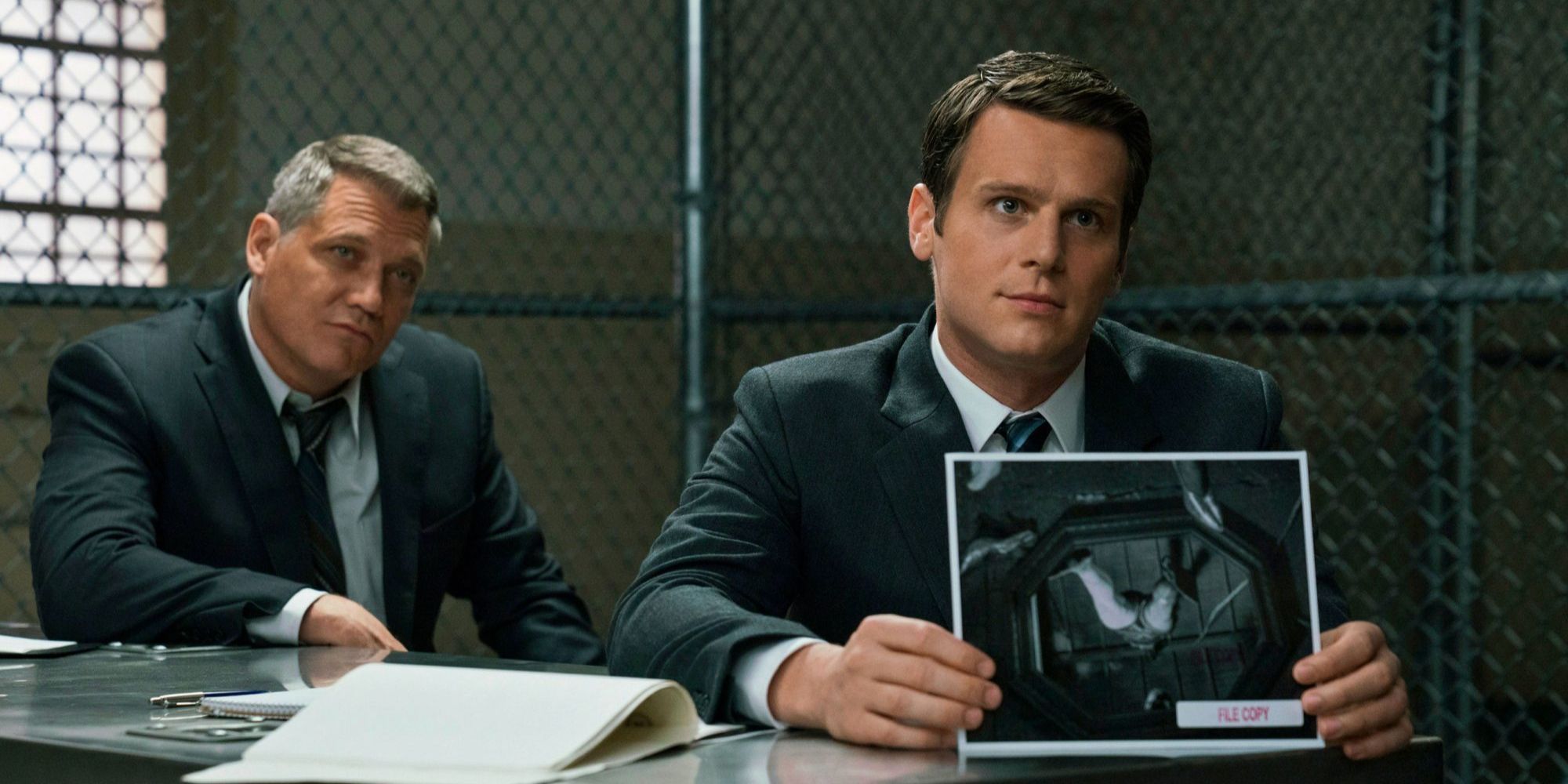 Holden Ford holds a crime scene photo while Bill Tench observes in Mindhunter