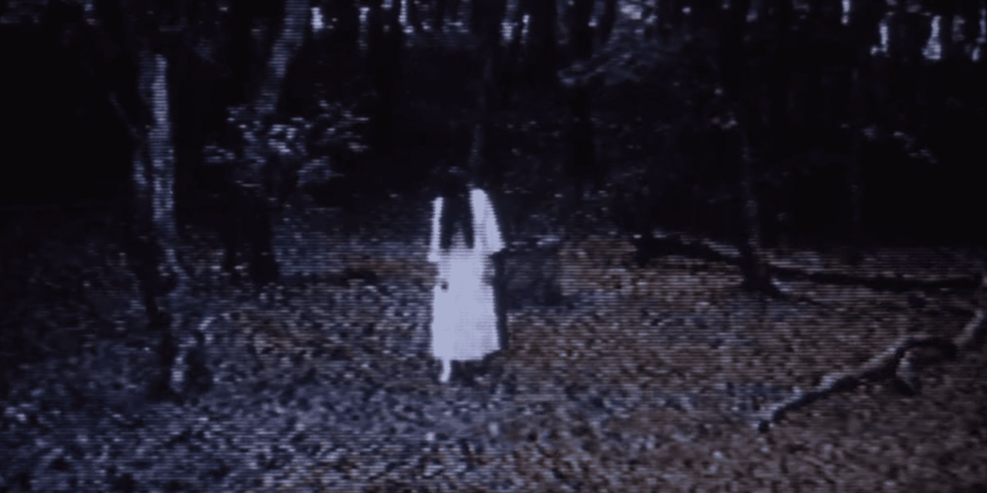 Rie Ino dans le rôle de Sadako, une jeune femme en blanc avec des cheveux noirs sur le visage dans les bois, de 'Ringu'
