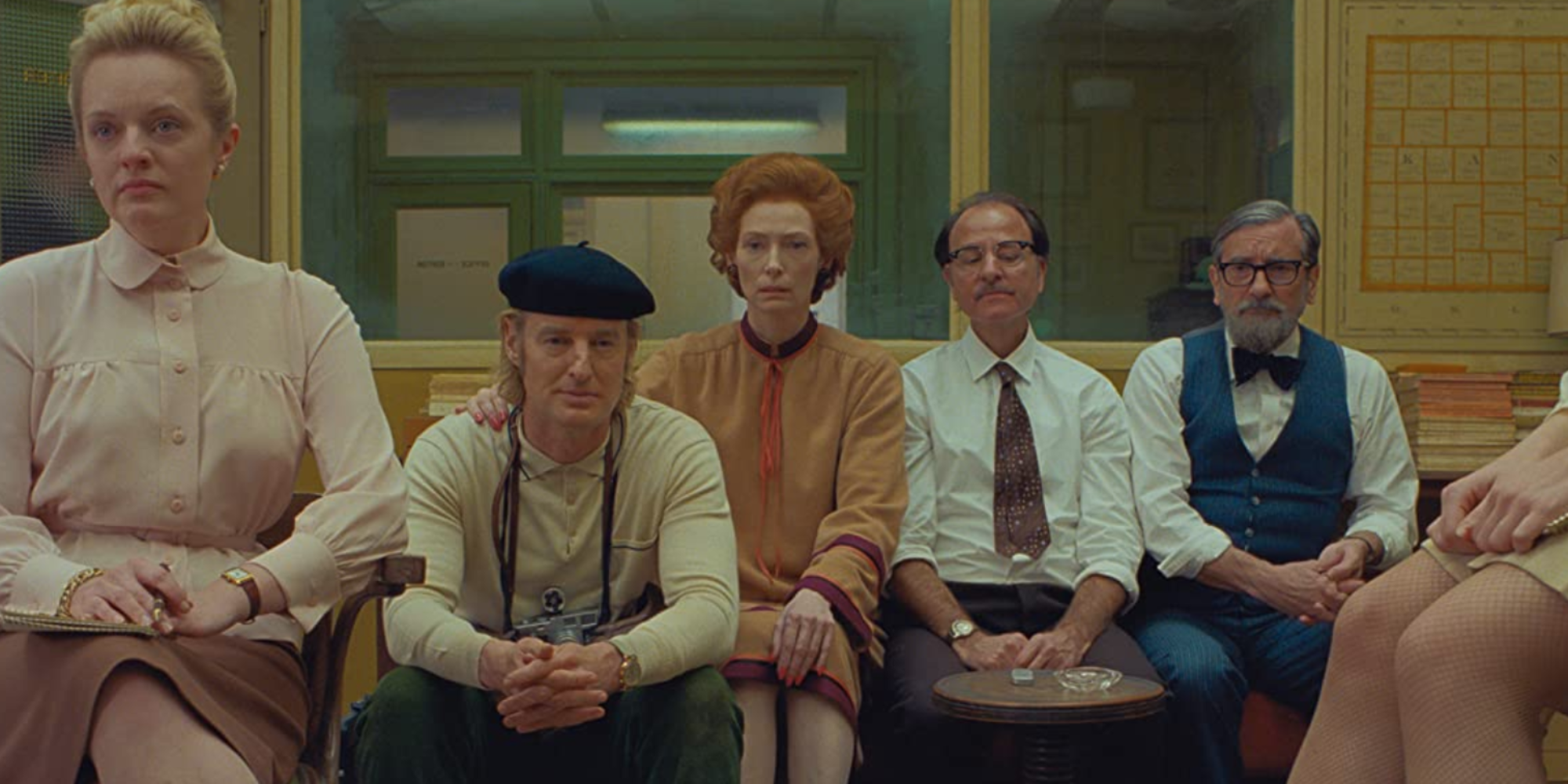 A group of characters sitting together in a couch in The French Dispatch.