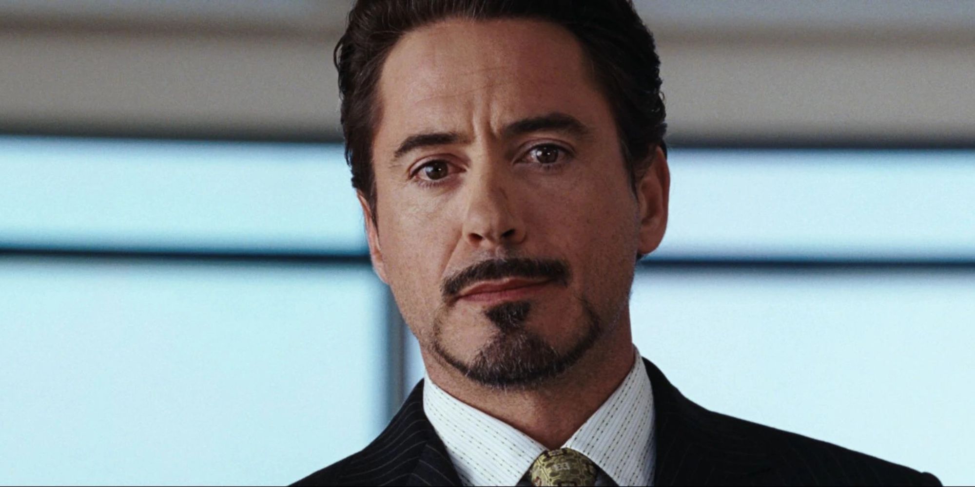 Robert Downey Jr. as Tony Stark with a slight smile at a press conference in Iron Man.