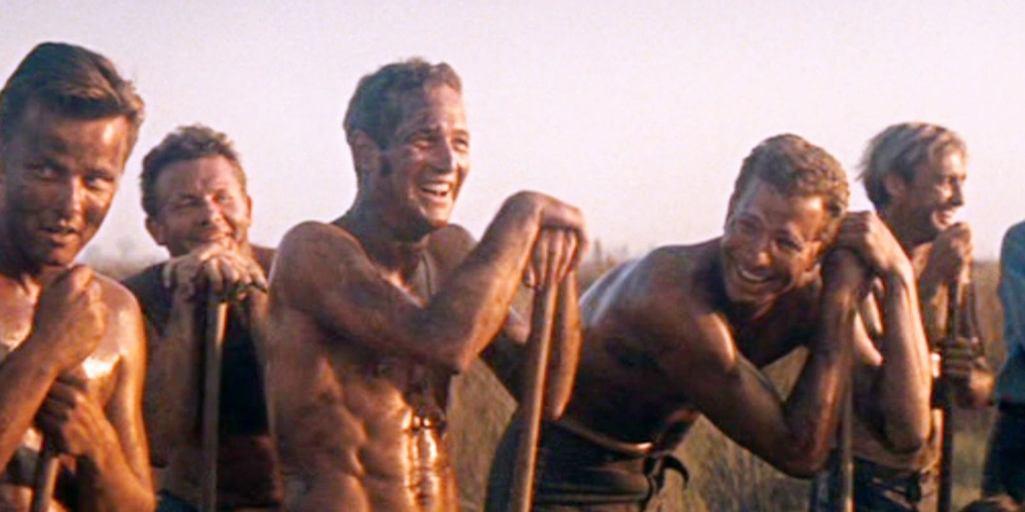 A barechested Luke laughing with other inmates while standing outside in the film Cool Hand Luke.