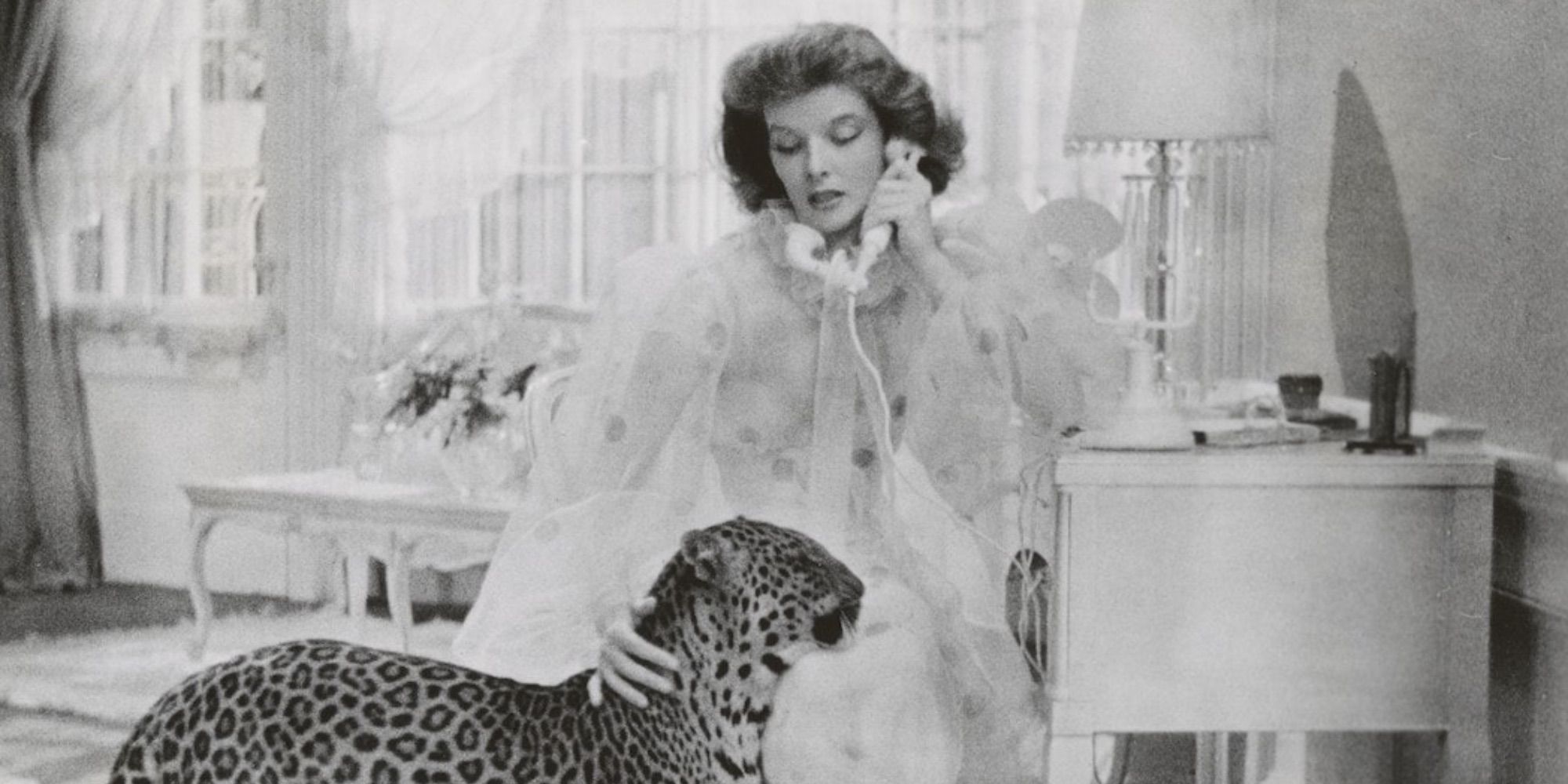 Katharine Hepburn interpreta a Susan Vance, quien acaricia a su mascota, un leopardo, mientras habla por teléfono en 