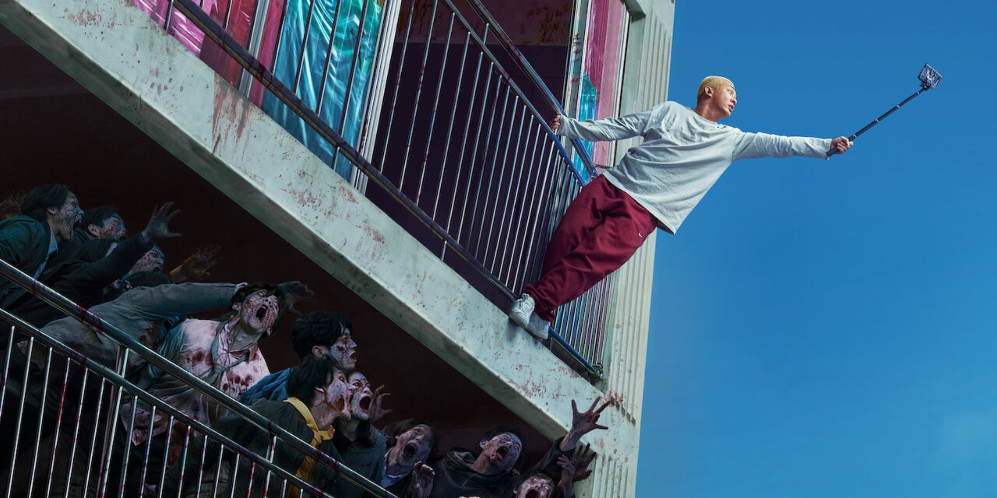 A man stands on a balcony rail to take a selfie with a horde of zombies in #Alive.