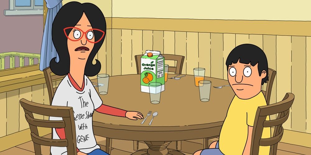 Linda and Gene sit at the kitchen table. Linda wears a hand drawn shirt that says The Gene Show With Gene.